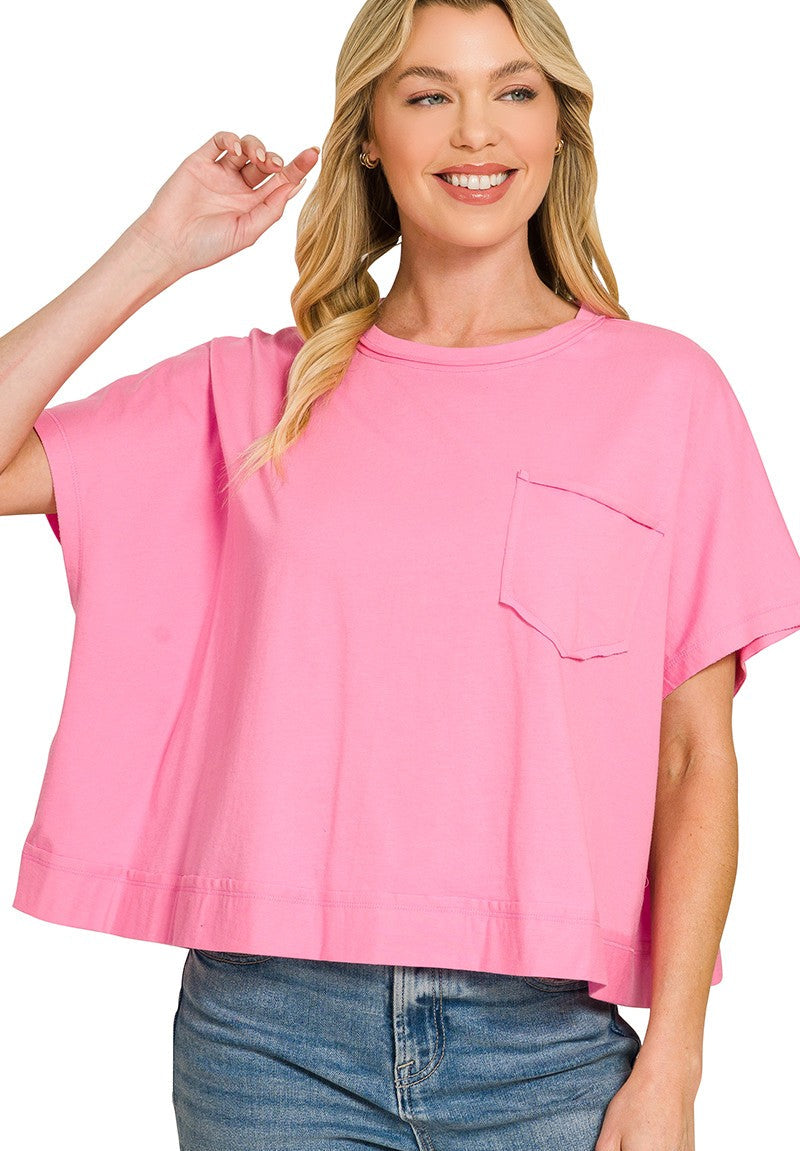 A woman wearing a bright pink short-sleeve crop top with a chest pocket, paired with blue jeans, against a plain white background.