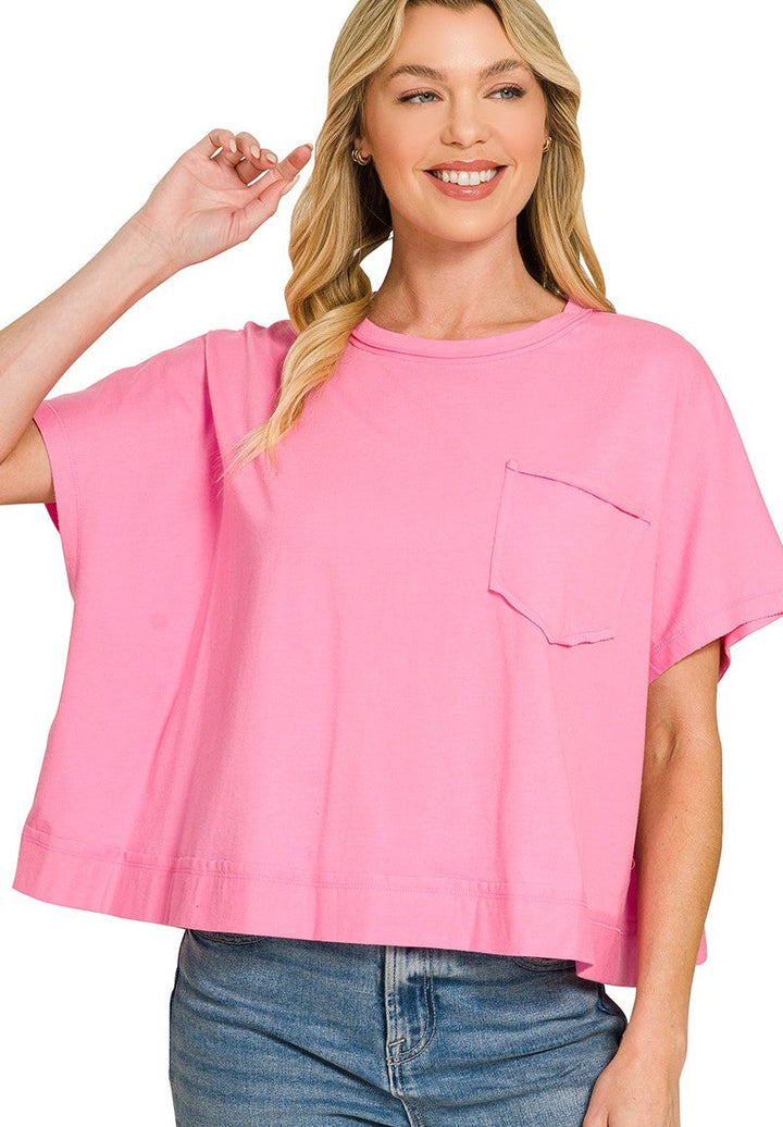 A woman wearing a bright pink short-sleeve crop top with a chest pocket, paired with blue jeans, against a plain white background.
