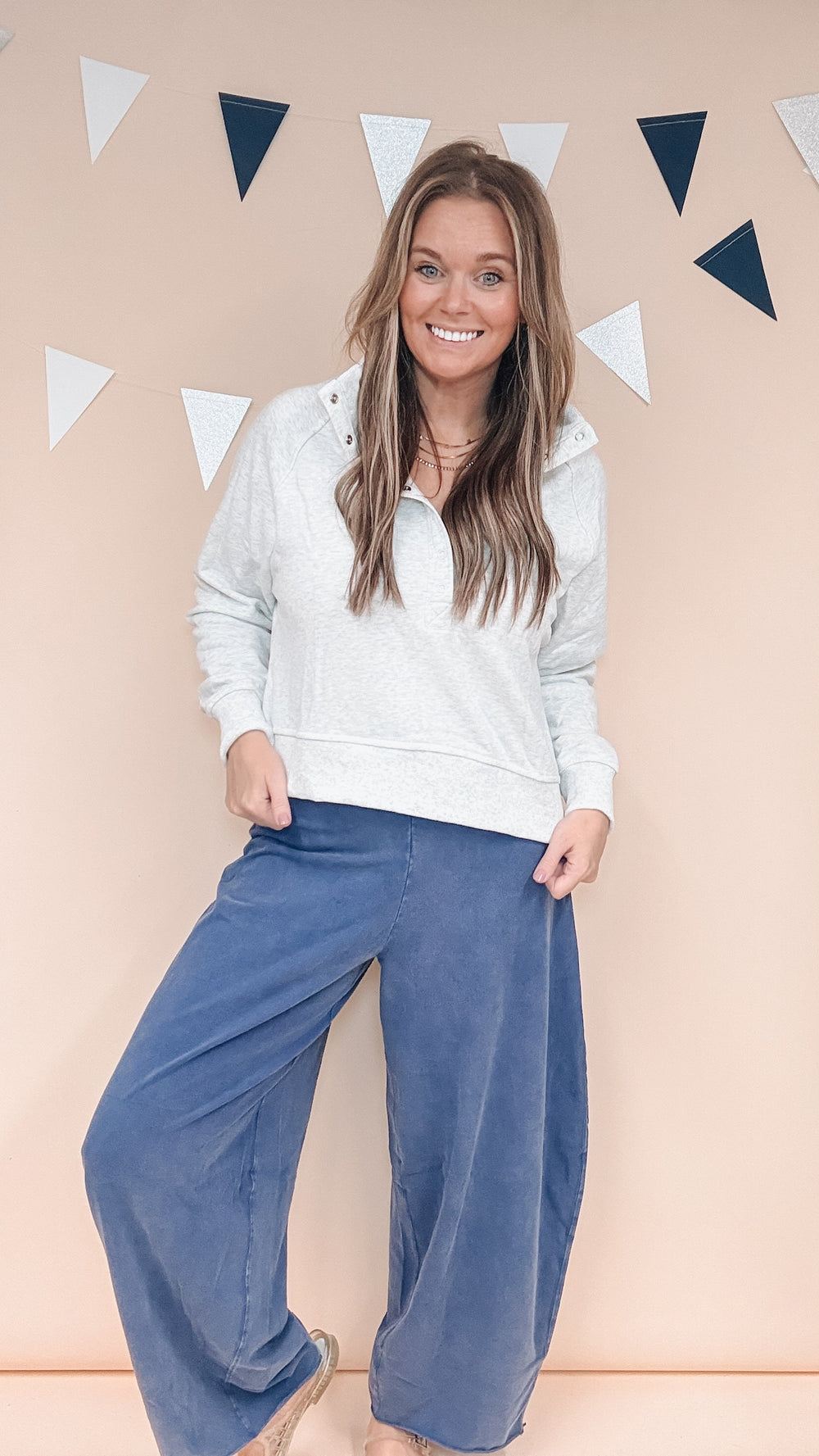 Woman wearing grey snap collar sweatshirt and navy blue pants on plain background