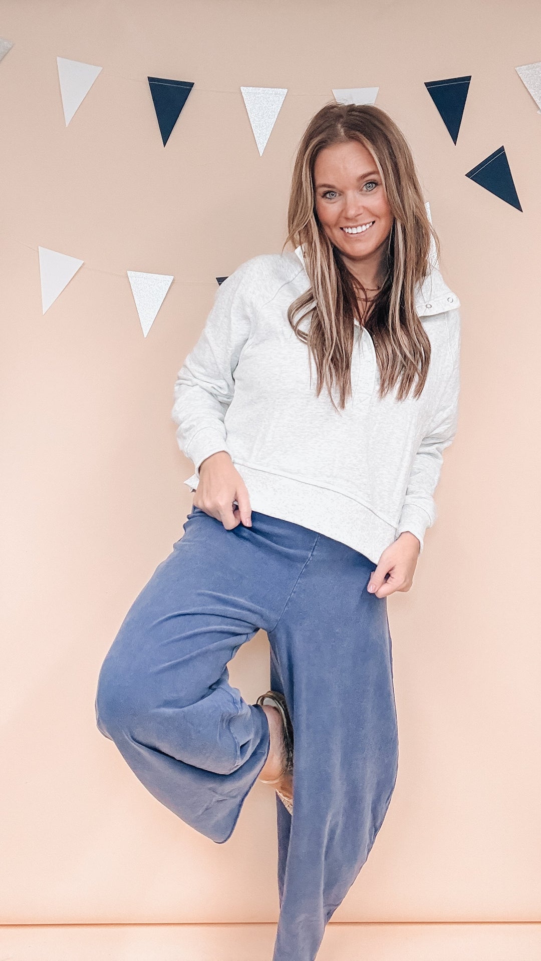 Woman wearing grey sweatshirt and navy blue pants on plain background