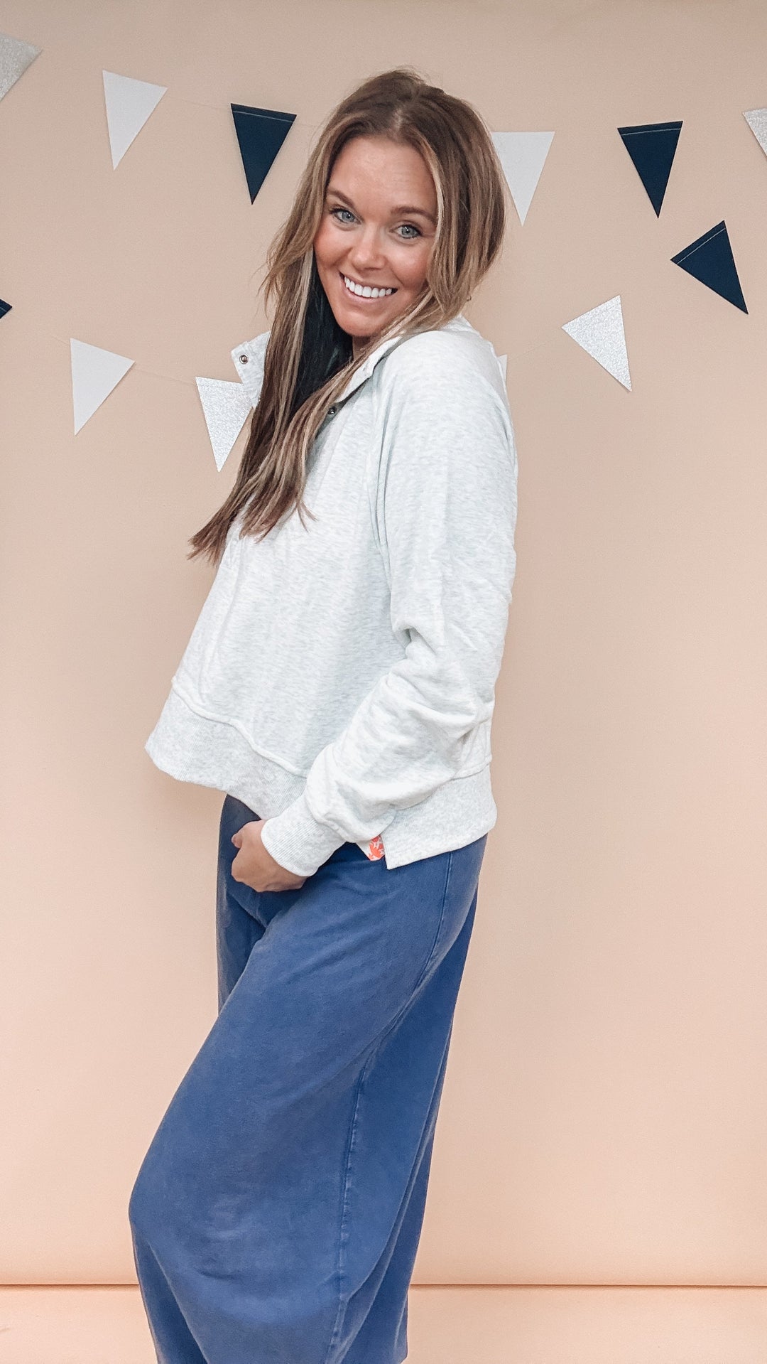 Woman wearing grey sweatshirt and navy blue pants on plain background