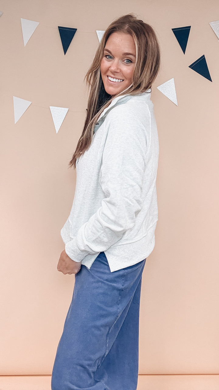 Woman wearing grey sweatshirt with navy blue pants on plain background