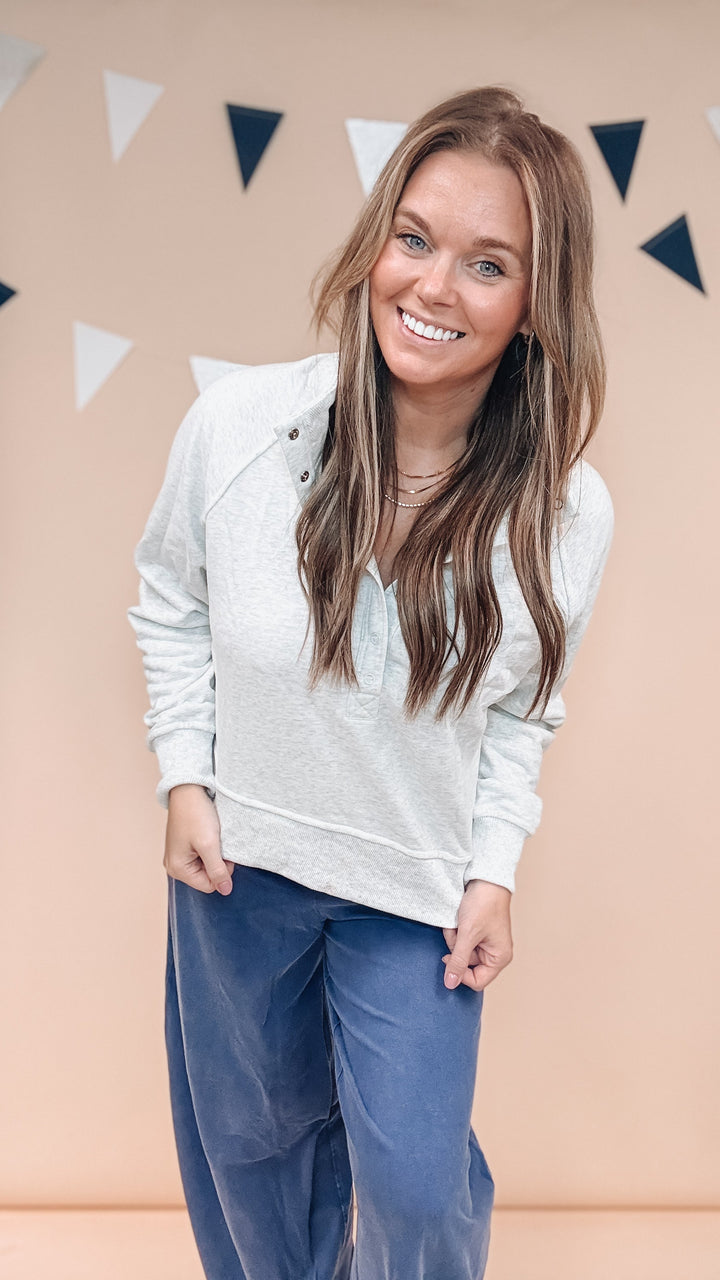 Woman wearing grey sweatshirt and navy blue pants on plain background