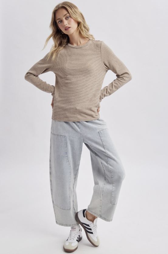 A woman modeling a beige ribbed long-sleeve knit top and wide-leg light-wash jeans with white sneakers, standing against a light gray studio background.