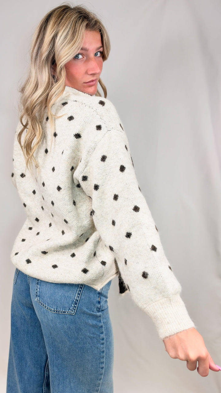Woman wearing oatmeal cardigan with brown polka dots and jeans on plain background