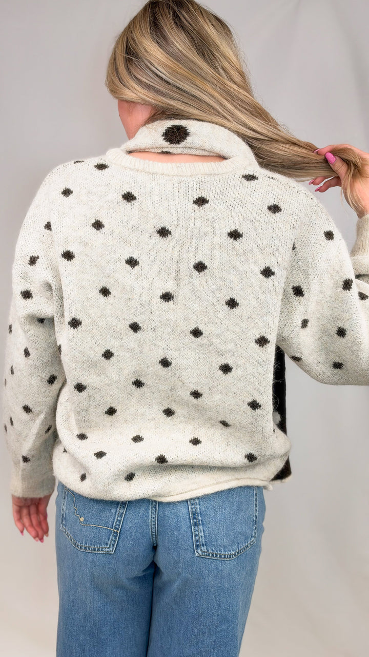 Woman shown from back wearing oatmeal cardigan with brown polka dots and matching scarf with jeans on plain background