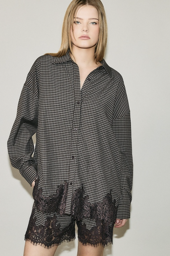 A woman modeling a black and white gingham button-up shirt with black lace trim at the hem, paired with matching black lace shorts, against a plain light gray studio background.