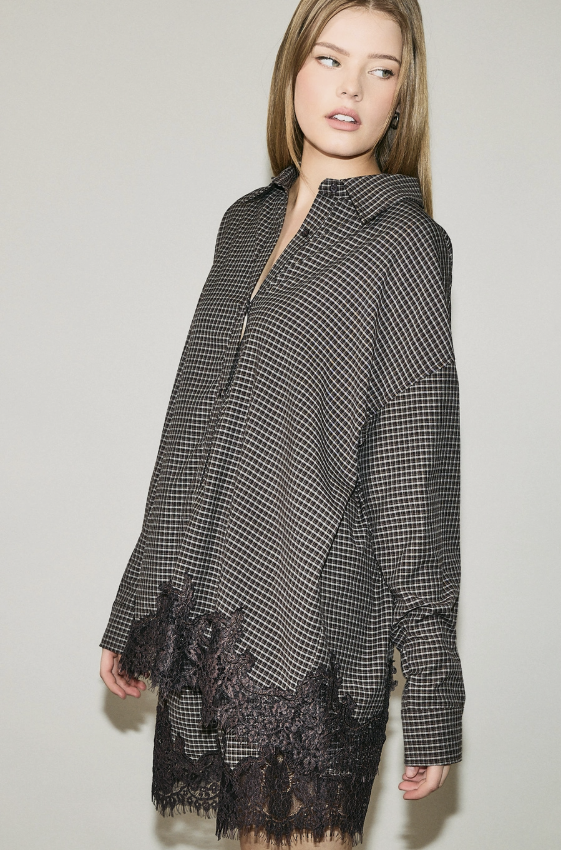 A woman wearing a black and white micro-check patterned cardigan with black lace trim at the hem and cuffs, photographed against a neutral light gray studio background.