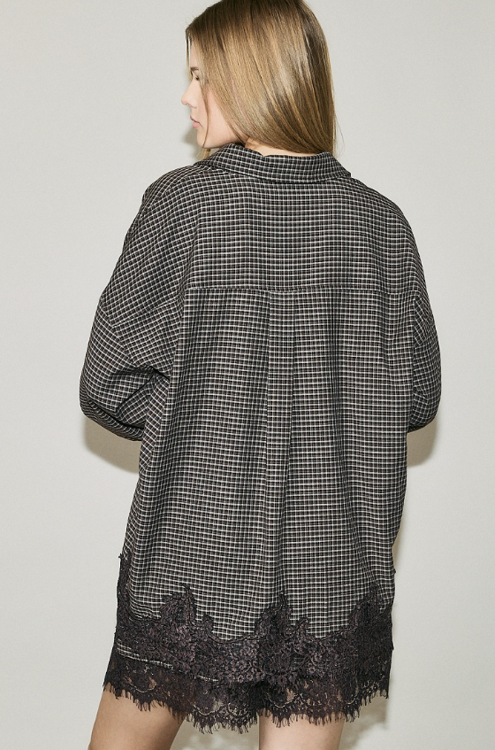 A woman shown from the back wearing an oversized black and white gingham shirt with a black lace hem, set against a plain light gray background.