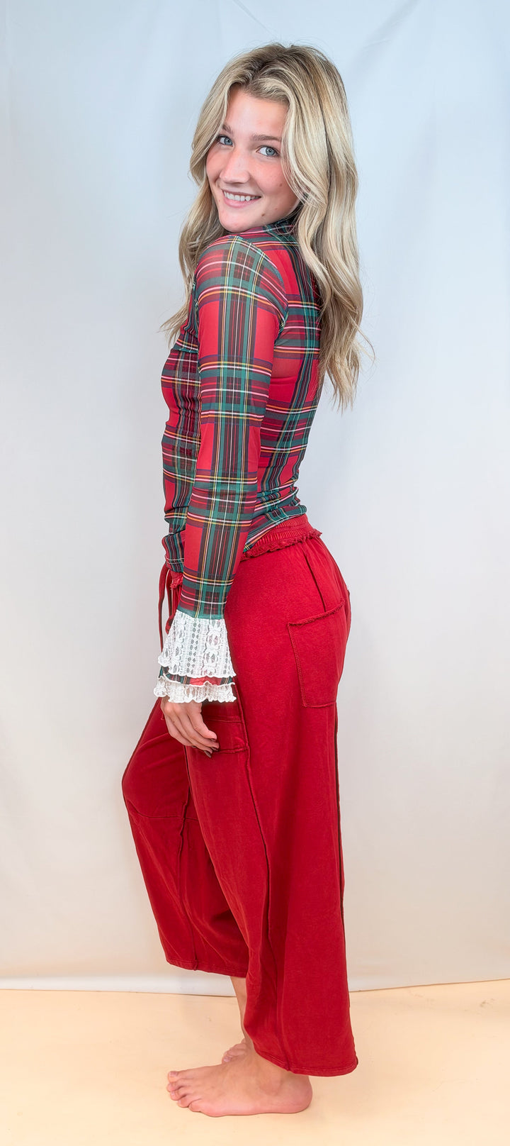 Woman shown from side view wearing red tartan sheer top with red pants on plain background