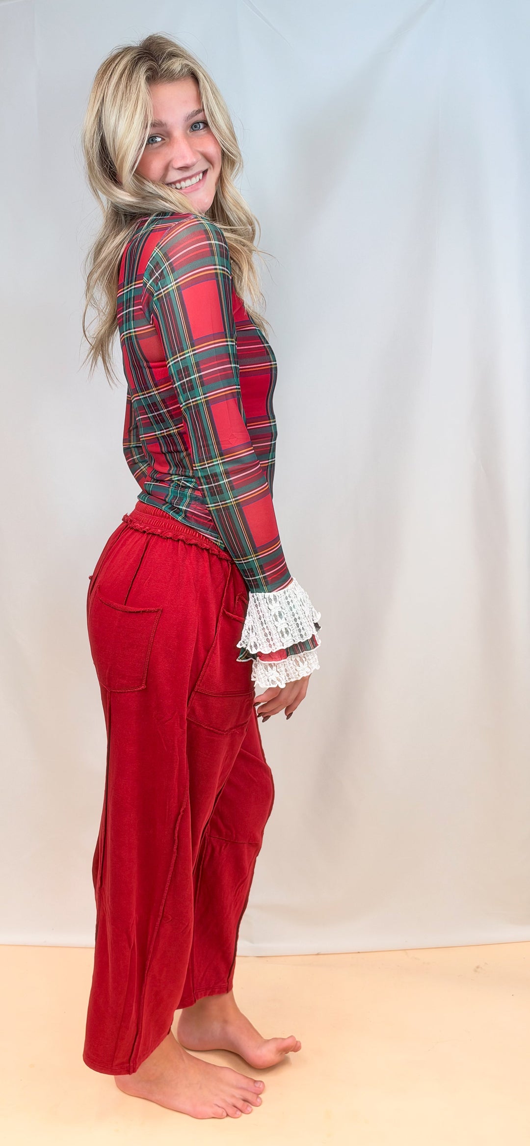 Woman shown from side view wearing red tartan sheer top with red pants on plain background