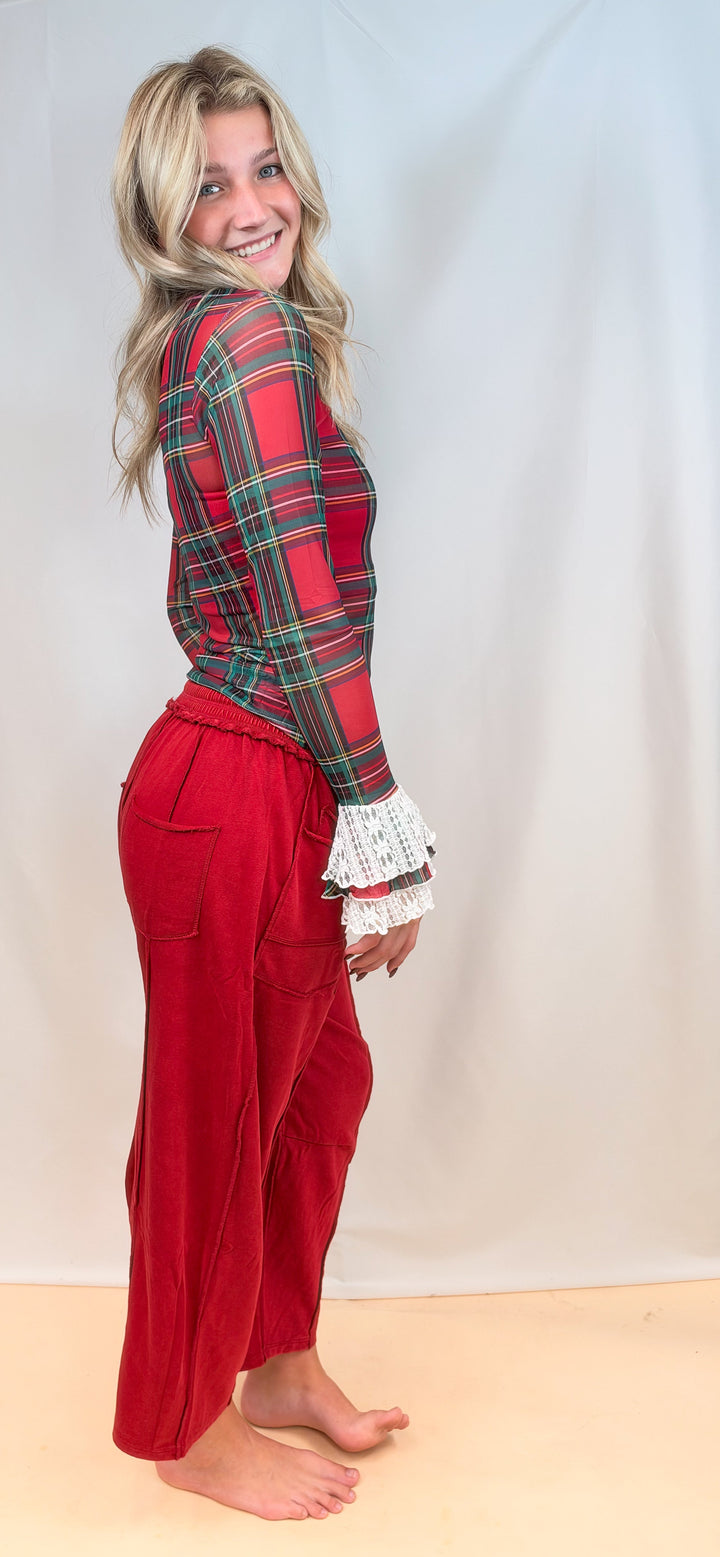 Woman shown from side view wearing red tartan sheer top with red pants on plain background