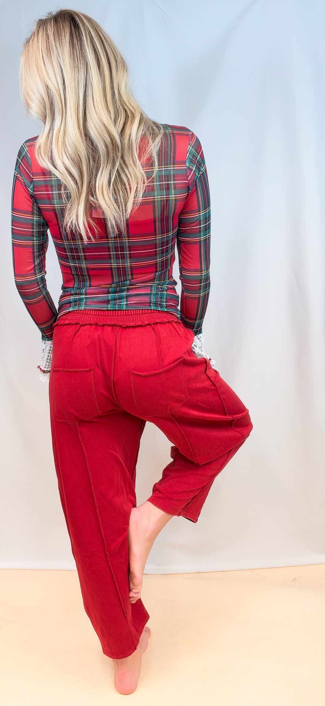 Woman shown from back view wearing red tartan sheer top with red pants on plain background