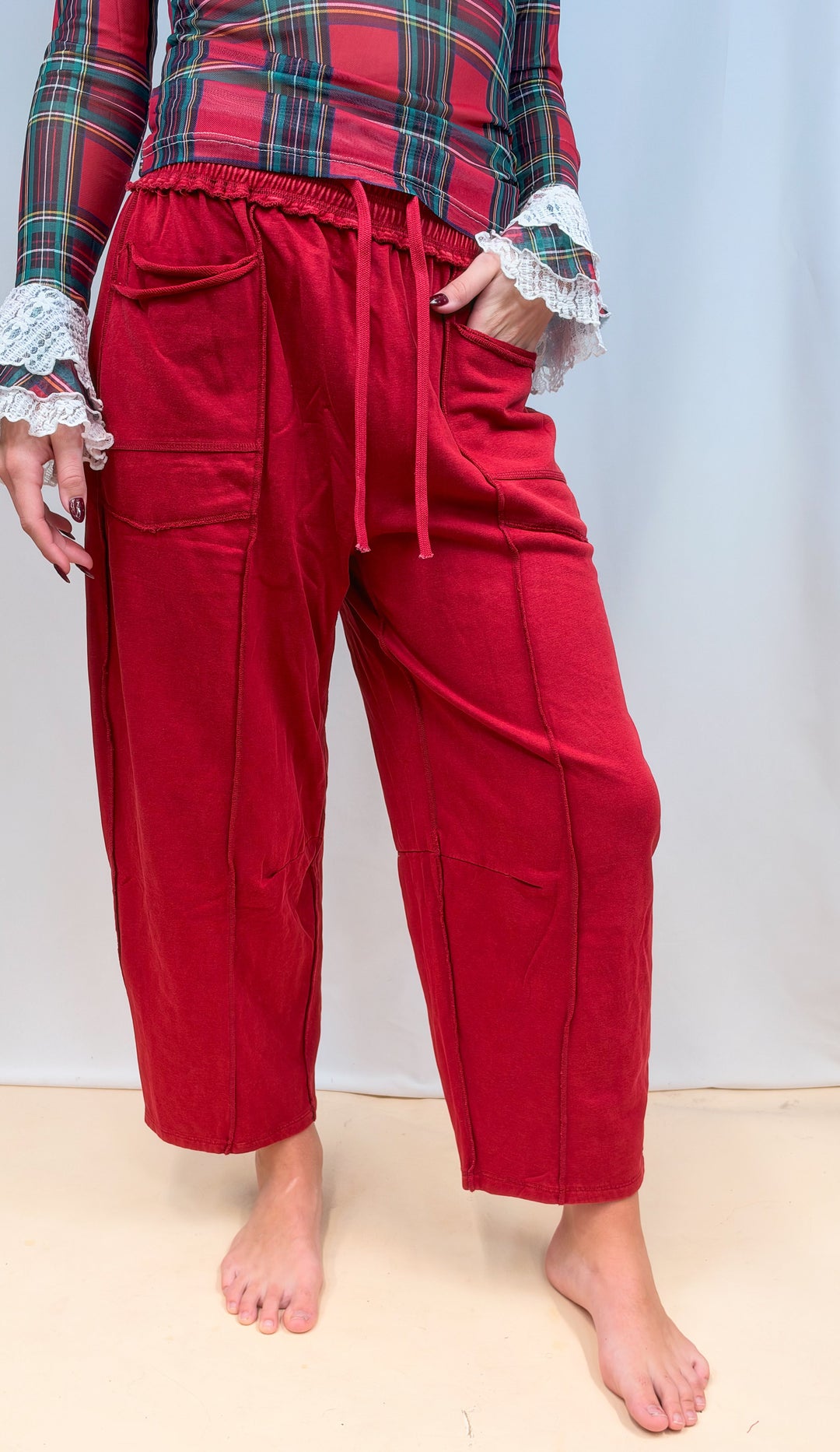 Woman shown from waist down wearing red barrel style sweatpants on plain background
