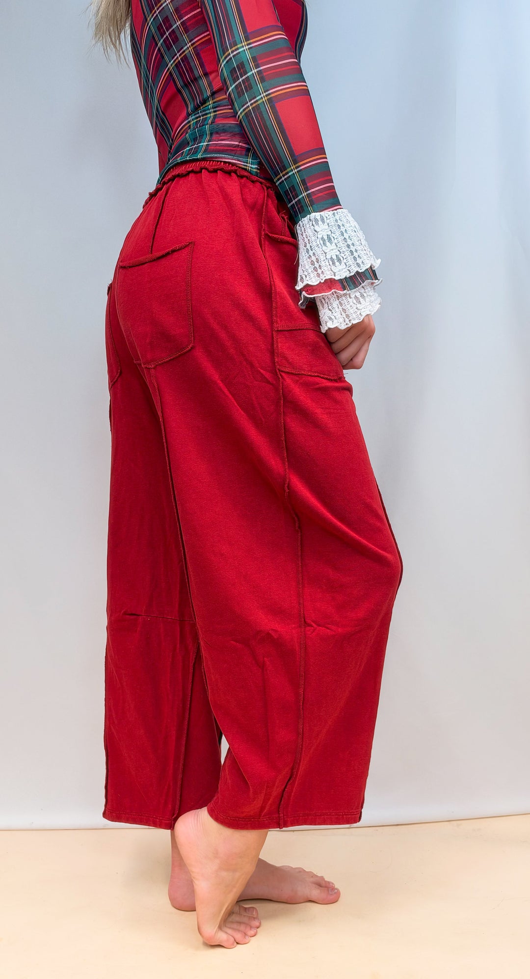 Woman shown from side view waist down wearing red barrel style sweatpants on plain background