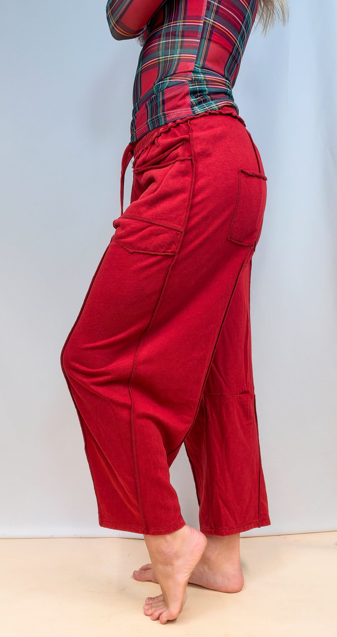 Woman shown from side view waist down wearing red barrel style sweatpants on plain background