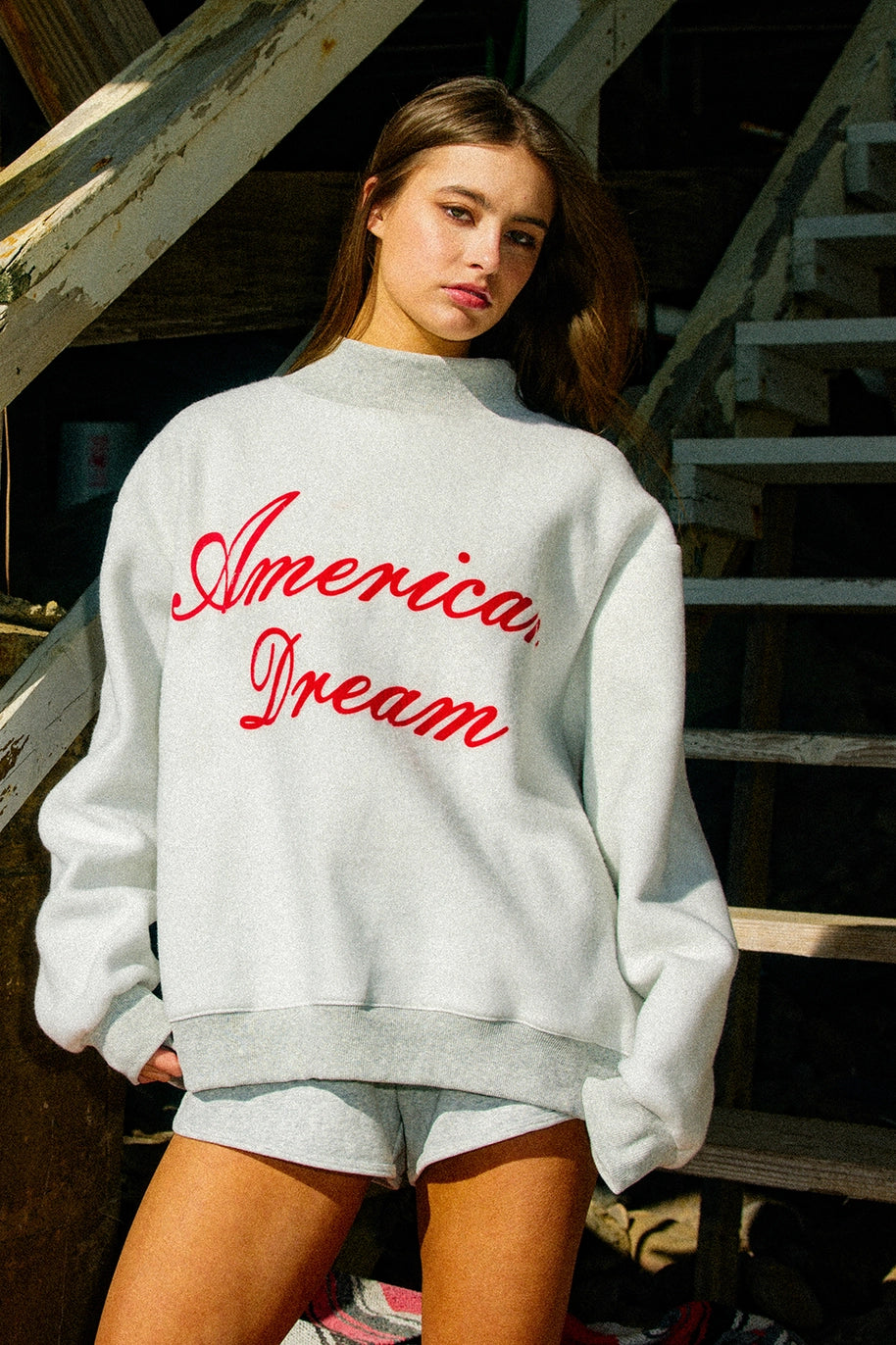 Person wearing a white sweatshirt with 'American Dream' in red text, standing on a staircase.