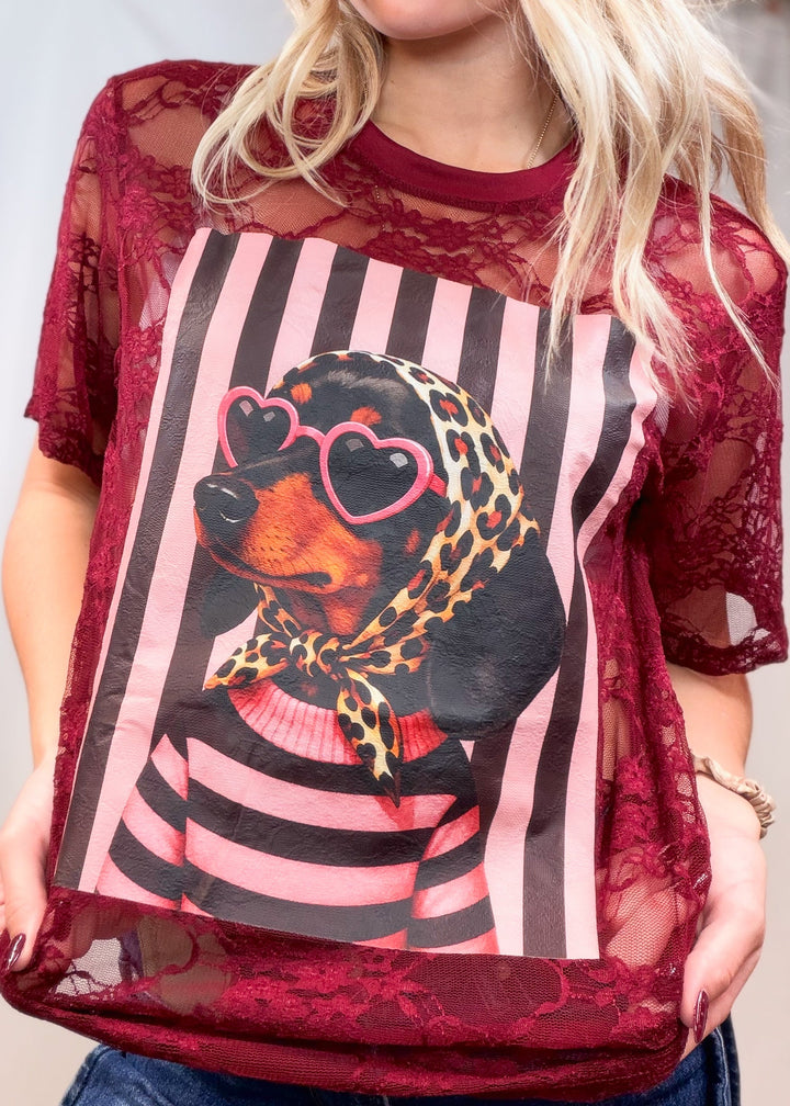 Woman wearing burgundy lace tee with doxie graphic on front on plain background