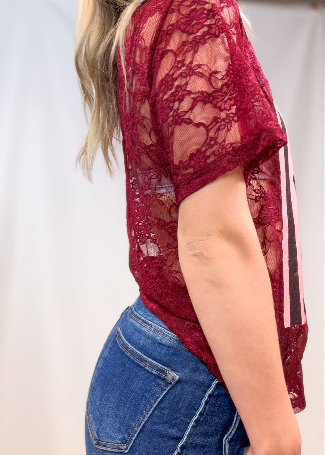 Woman wearing burgundy lace tee with denim jeans on plain background