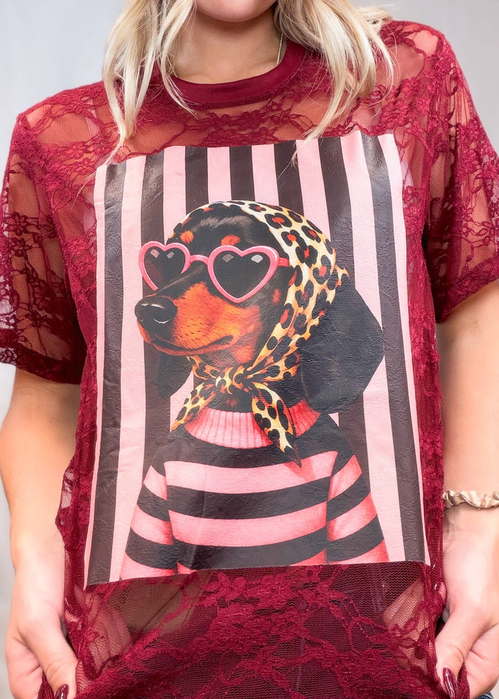 Woman wearing burgundy lace tee with doxie graphic on front on plain background