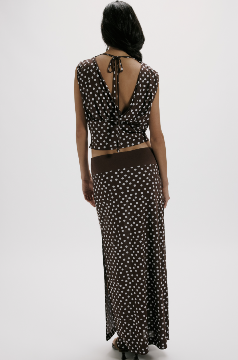 Woman wearing a brown and white polka dot dress with a tied back design on a white background