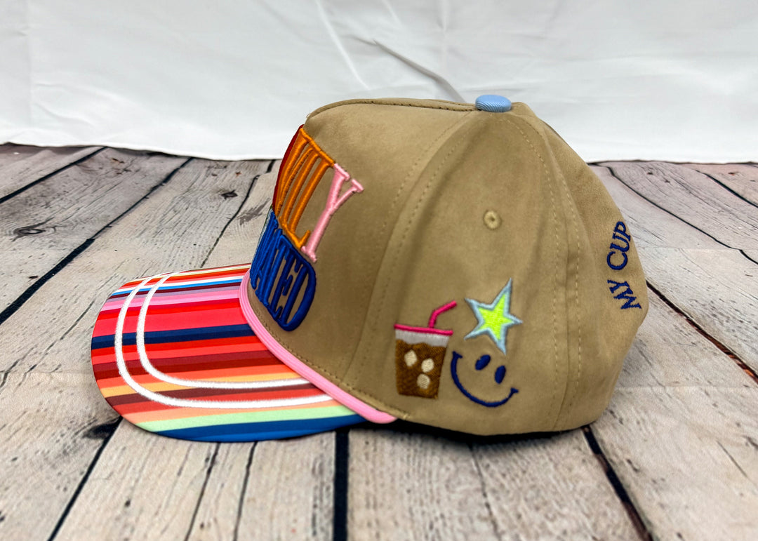Brown trucker hat on wooden floor with coffee, star and smile embroidery on side on white background