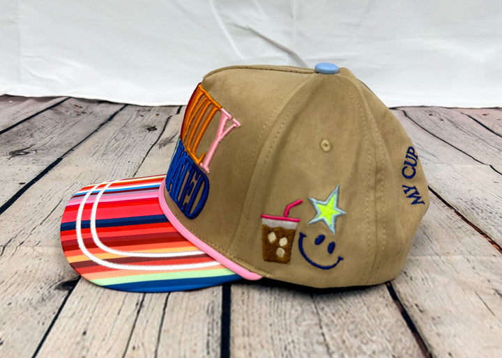 Brown trucker hat on wooden floor with coffee, star and smile embroidery on side on white background