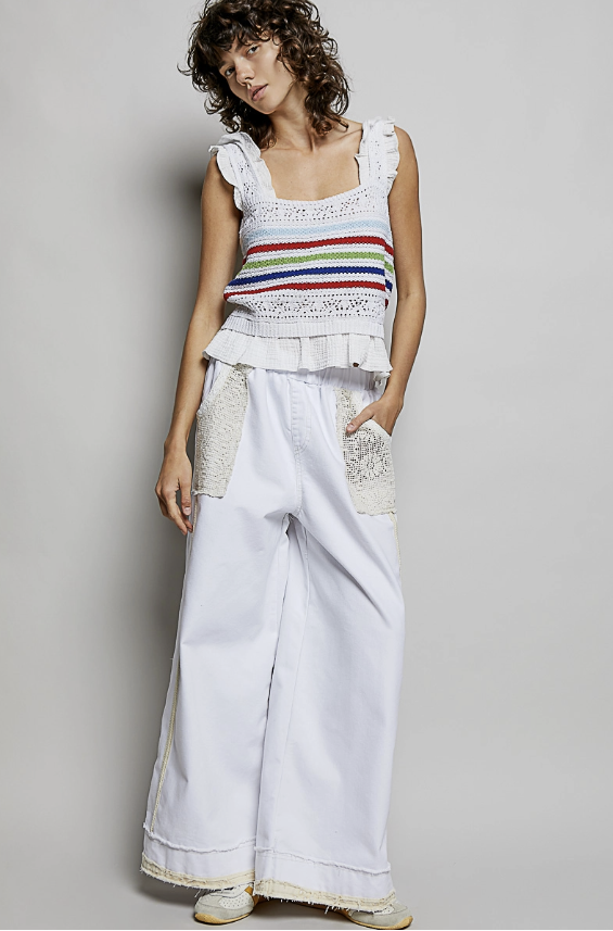 Woman wearing a colorful striped top and white pants against a plain background