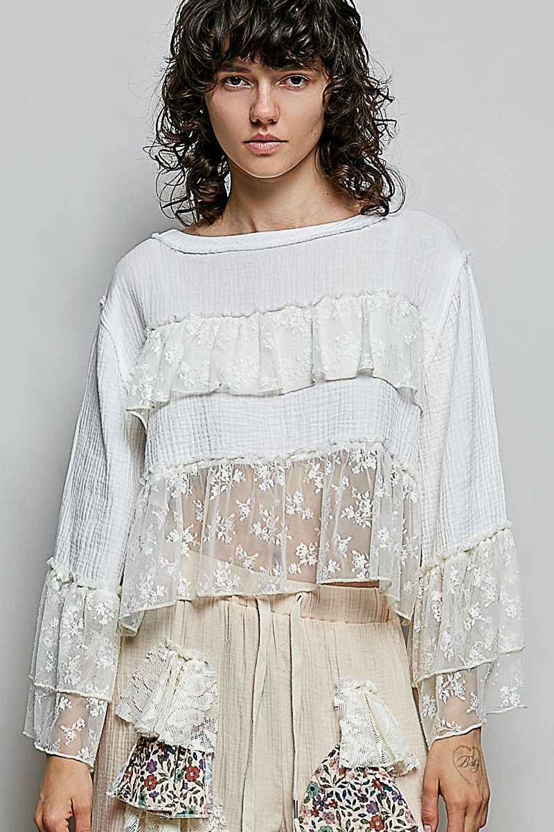 Woman wearing a layered, floral lace top against a plain background