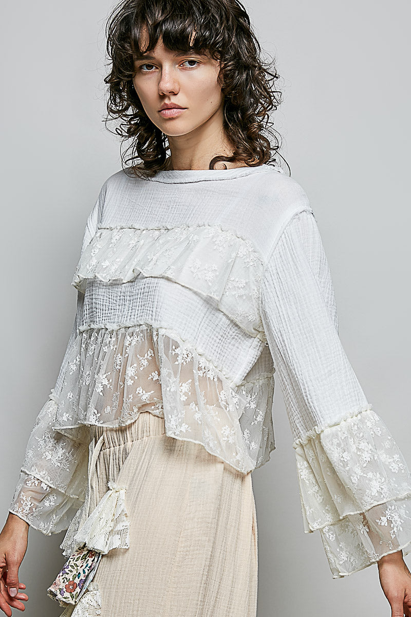 Woman wearing a layered white top with lace details on a gray background