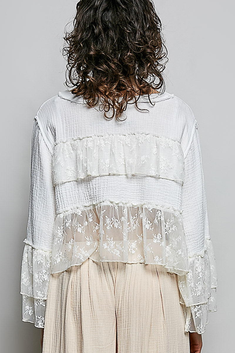 Person wearing a layered white lace top with sheer sleeves on a plain background