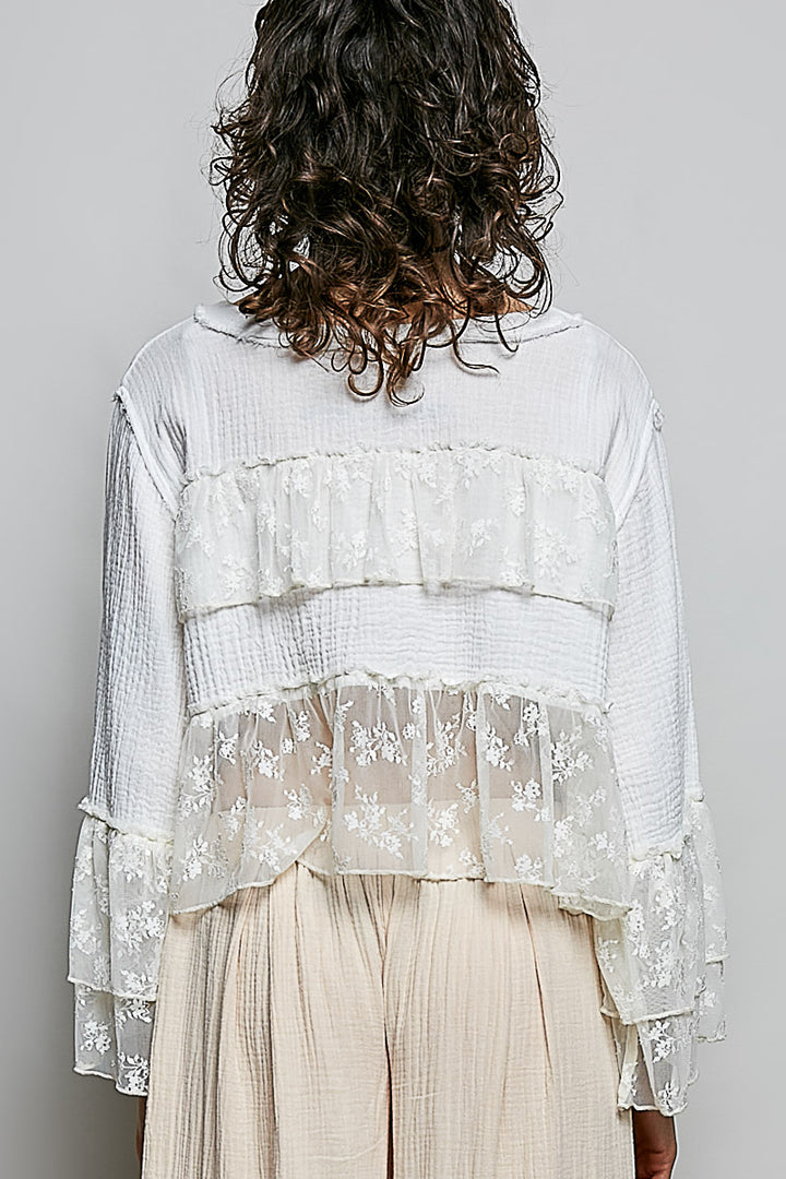 Person wearing a layered white lace top with sheer sleeves on a plain background