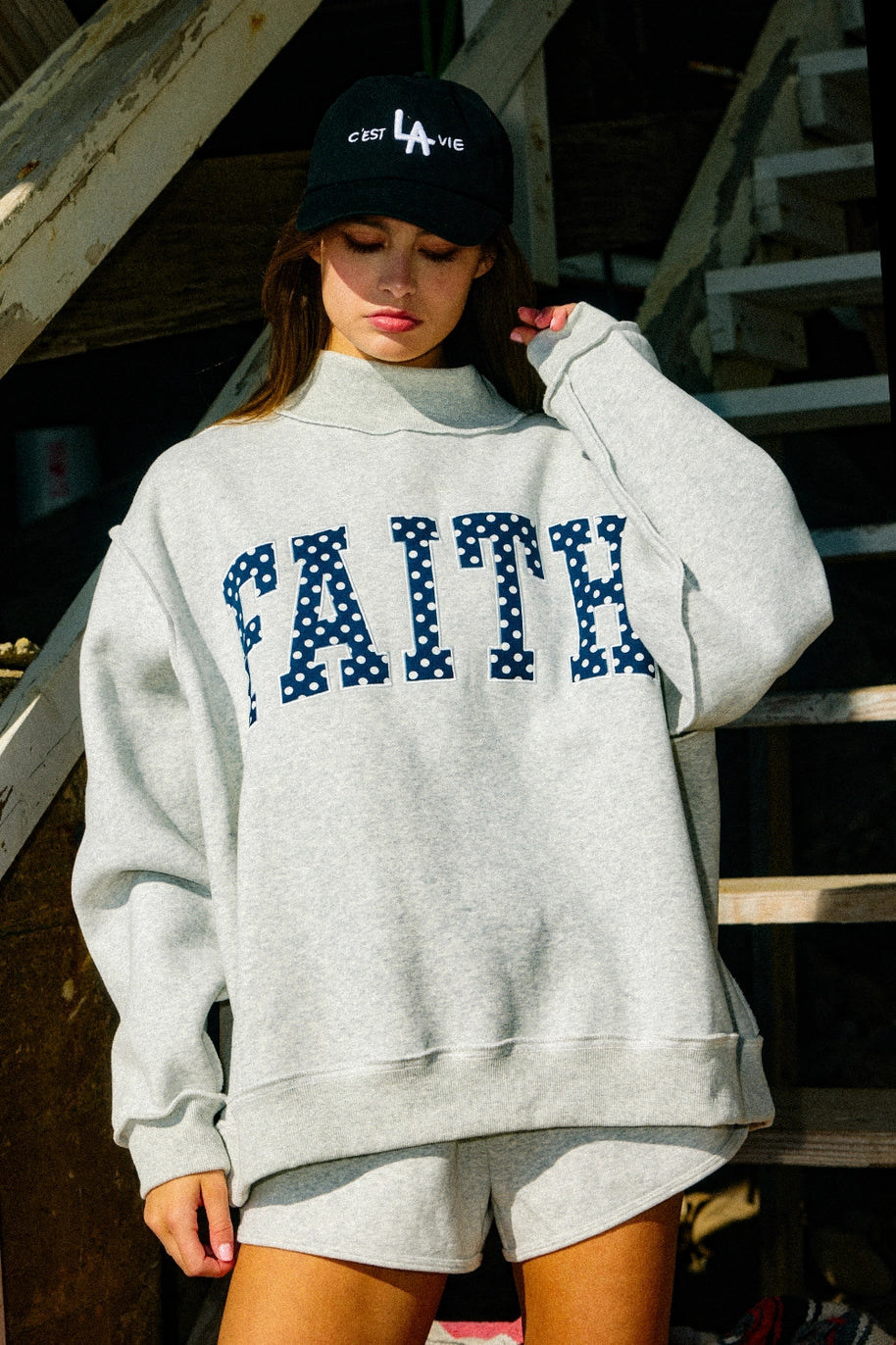 Woman wearing grey sweatshirt with "FAITH&