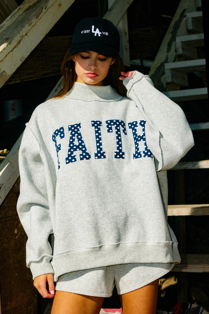 Woman wearing grey sweatshirt with "FAITH&
