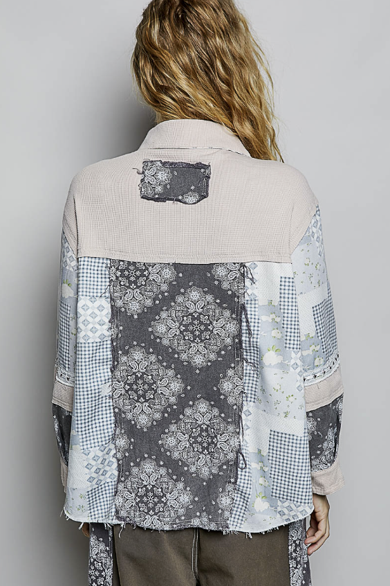 Person wearing a patchwork shirt with floral and geometric patterns on a plain background