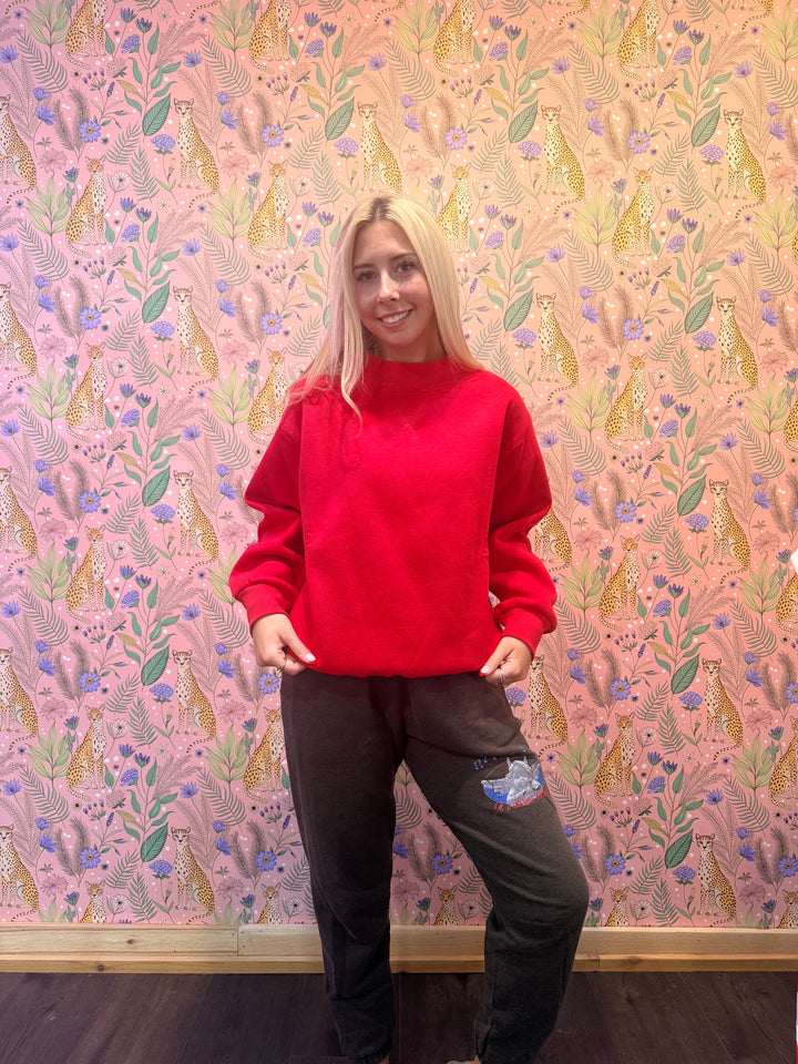 Person wearing a red hoodie and dark pants standing against a patterned wall.