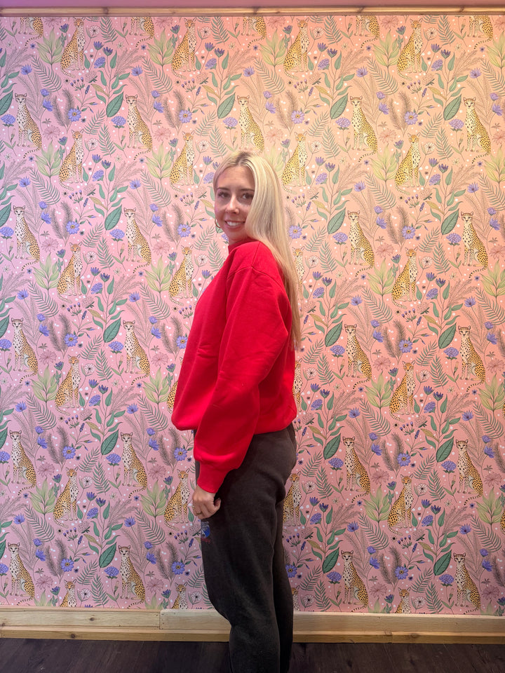 Woman wearing red sweatshirt and brown sweatpants in front of pink floral background