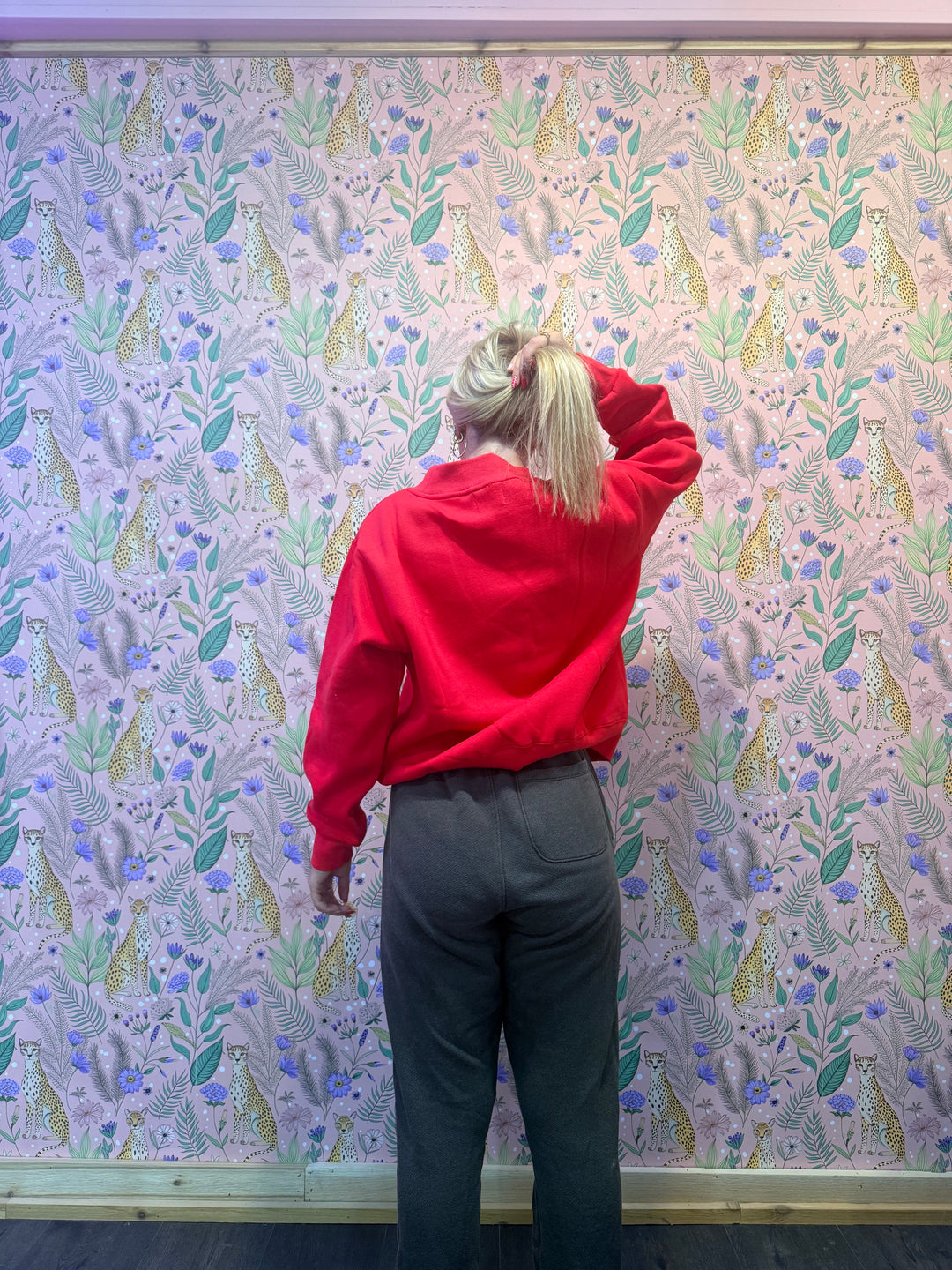 Person wearing a red hoodie and dark pants standing on a floral-patterned floor.