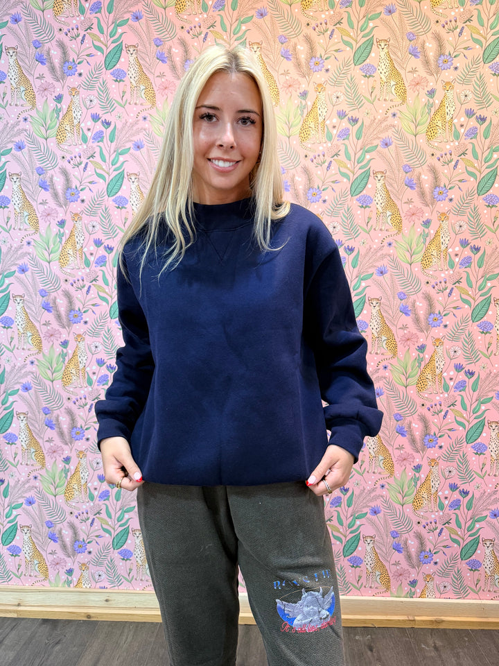 Person wearing a navy blue sweatshirt and dark pants in front of pink floral background