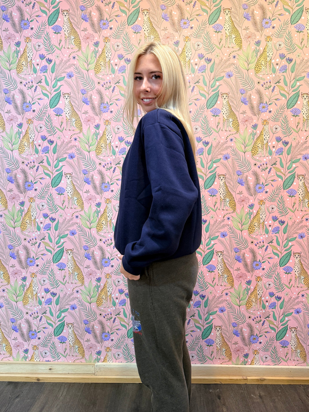 Person wearing a dark blue hoodie and brown pants in front of pink floral background
