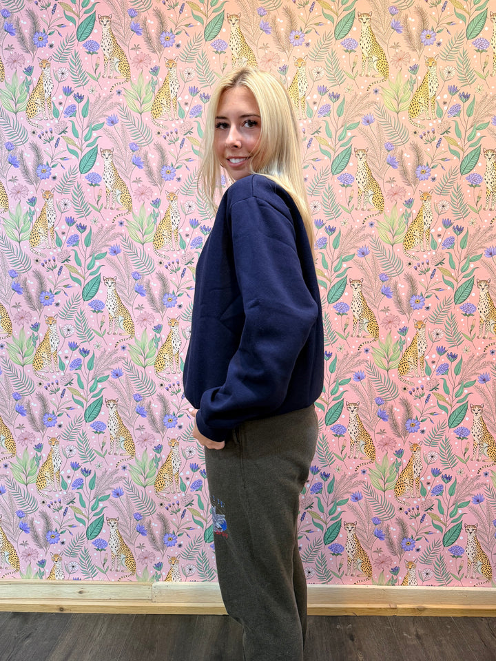 Person wearing a dark blue hoodie and brown pants in front of pink floral background