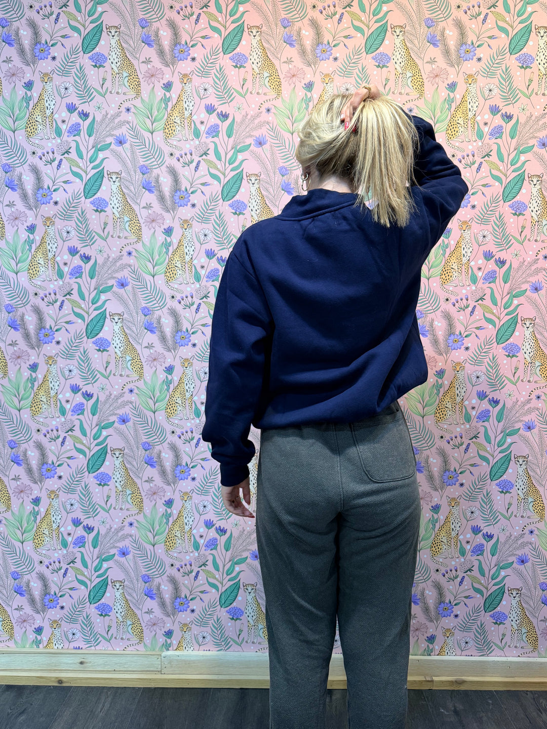 Woman wearing blue sweatshirt and brown pants in front of pink floral background