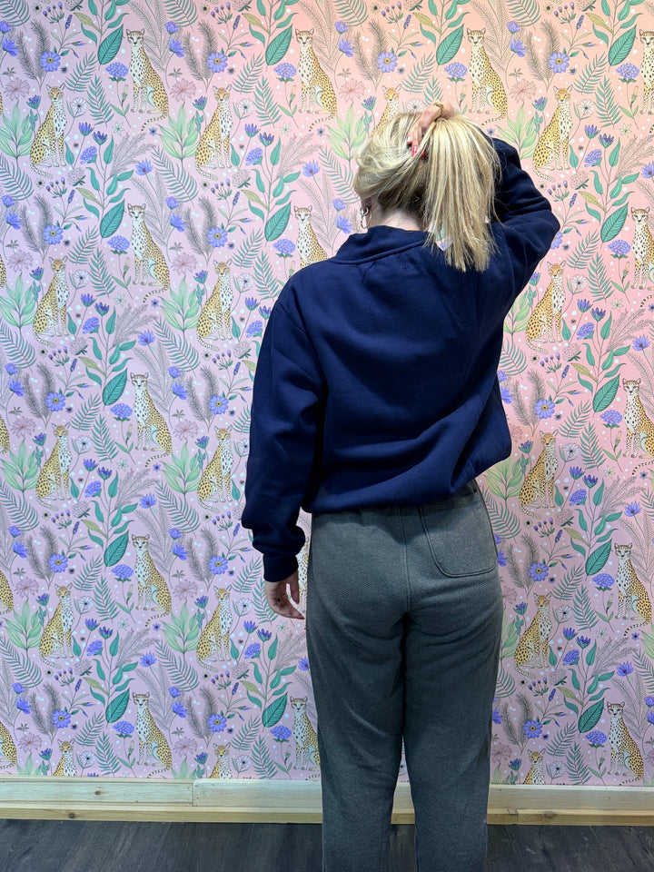 Woman wearing blue sweatshirt and brown pants in front of pink floral background