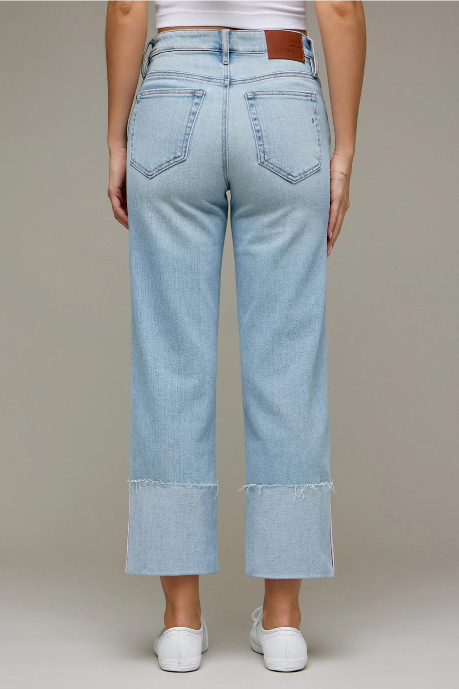 Back of woman wearing light wash denim pants on plain background