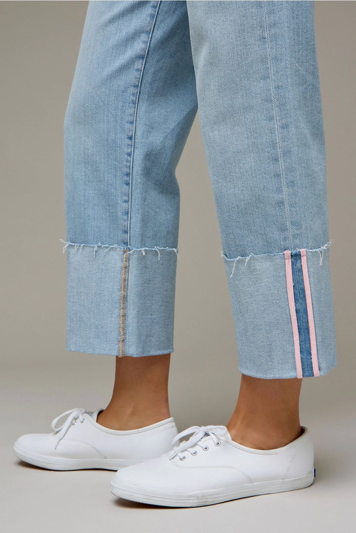 Woman wearing light wash denim pants with pink tape stripe on plain background