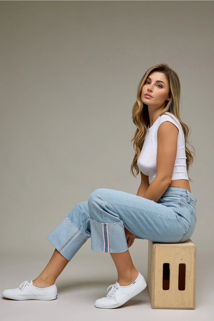 Woman sitting on a wooden block wearing a white top and light blue jeans against a plain background