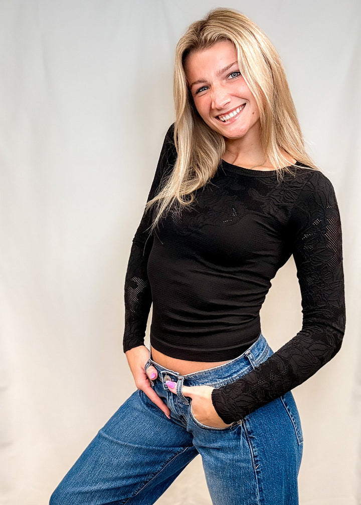 Woman wearing fitted black lace top with blue jeans on white background