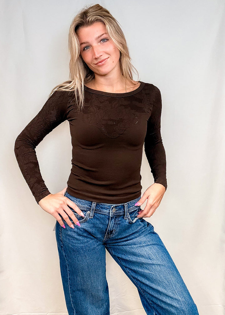 Woman wearing fitted brown lace top with blue jeans on white background