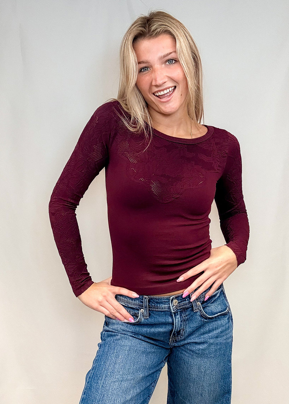 Woman wearing burgundy fitted lace top with blue jeans on white background