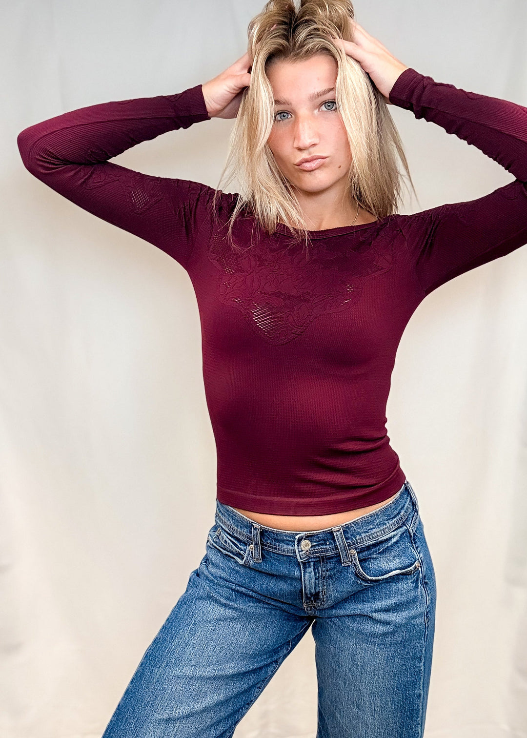 Woman wearing burgundy fitted lace top with blue jeans on white background